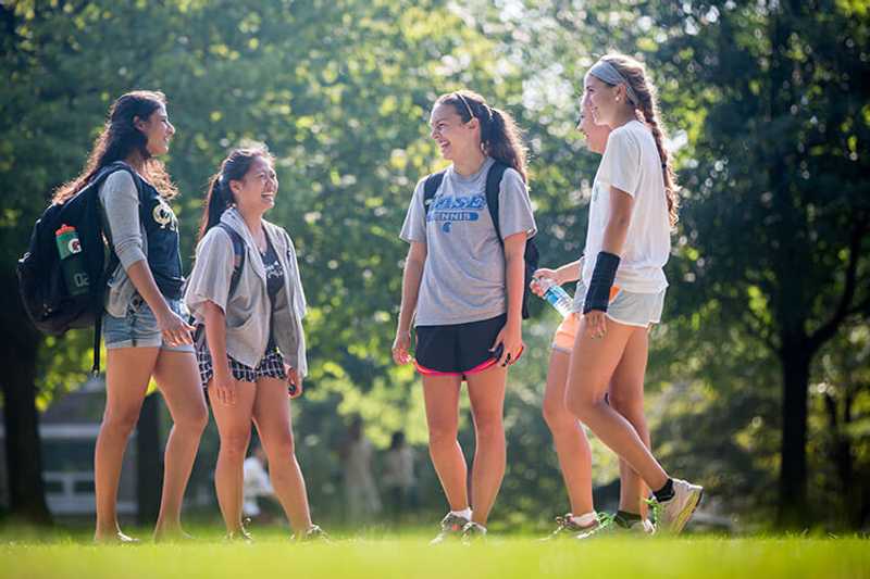 Photo of a group of Case Western Reserve University students standing in a circle outdoors on the quad, laughing
