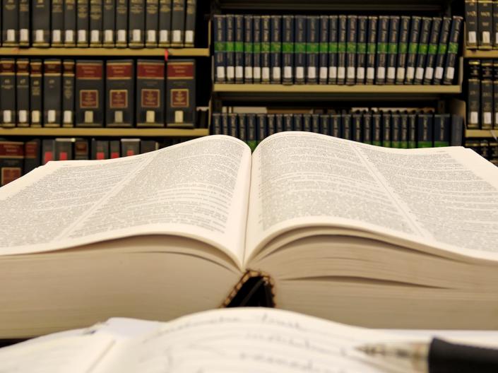 A book sitting open on a table with shelves of books in the background.