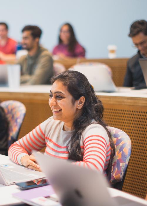 Student sits in a lecture smiling.