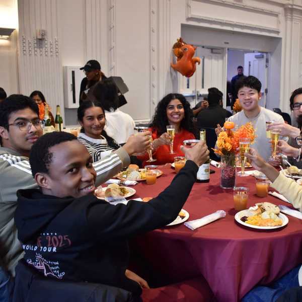 A group of eight students sitting around a table holding their glasses up to cheers.